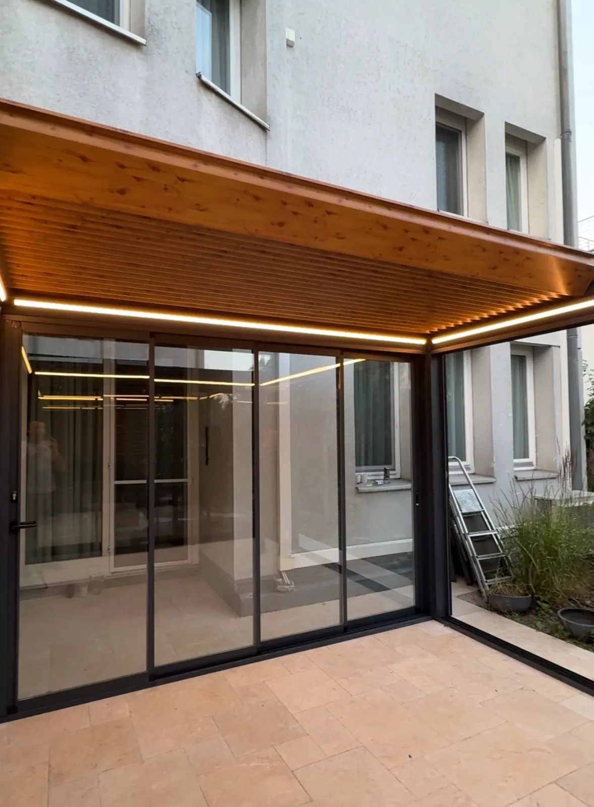 Bioklimatik-Pergola mit LED-Lichtband und Glaswänden an einem Wohnhaus