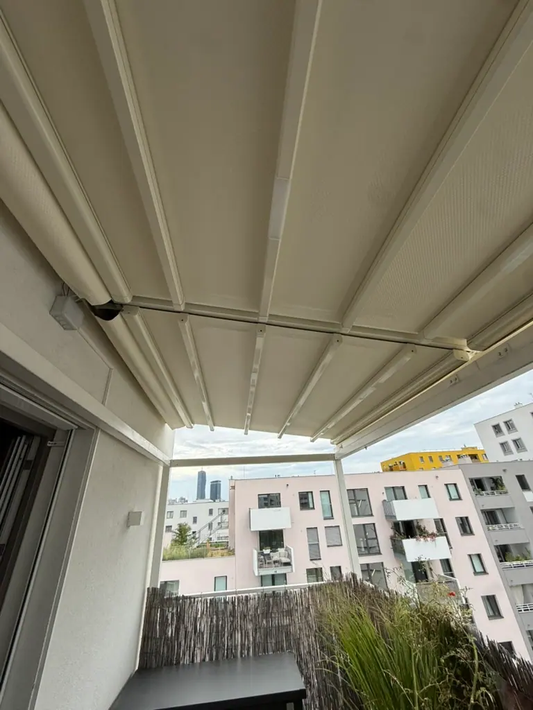 Blick unter das helle Faltdach einer Balkon-Pergola