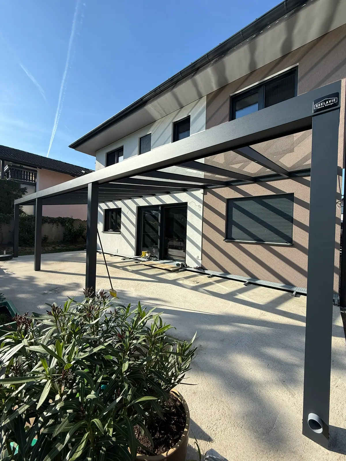 Terrassenüberdachung mit Glasdach an einem Einfamilienhaus, vorne ein Oleander