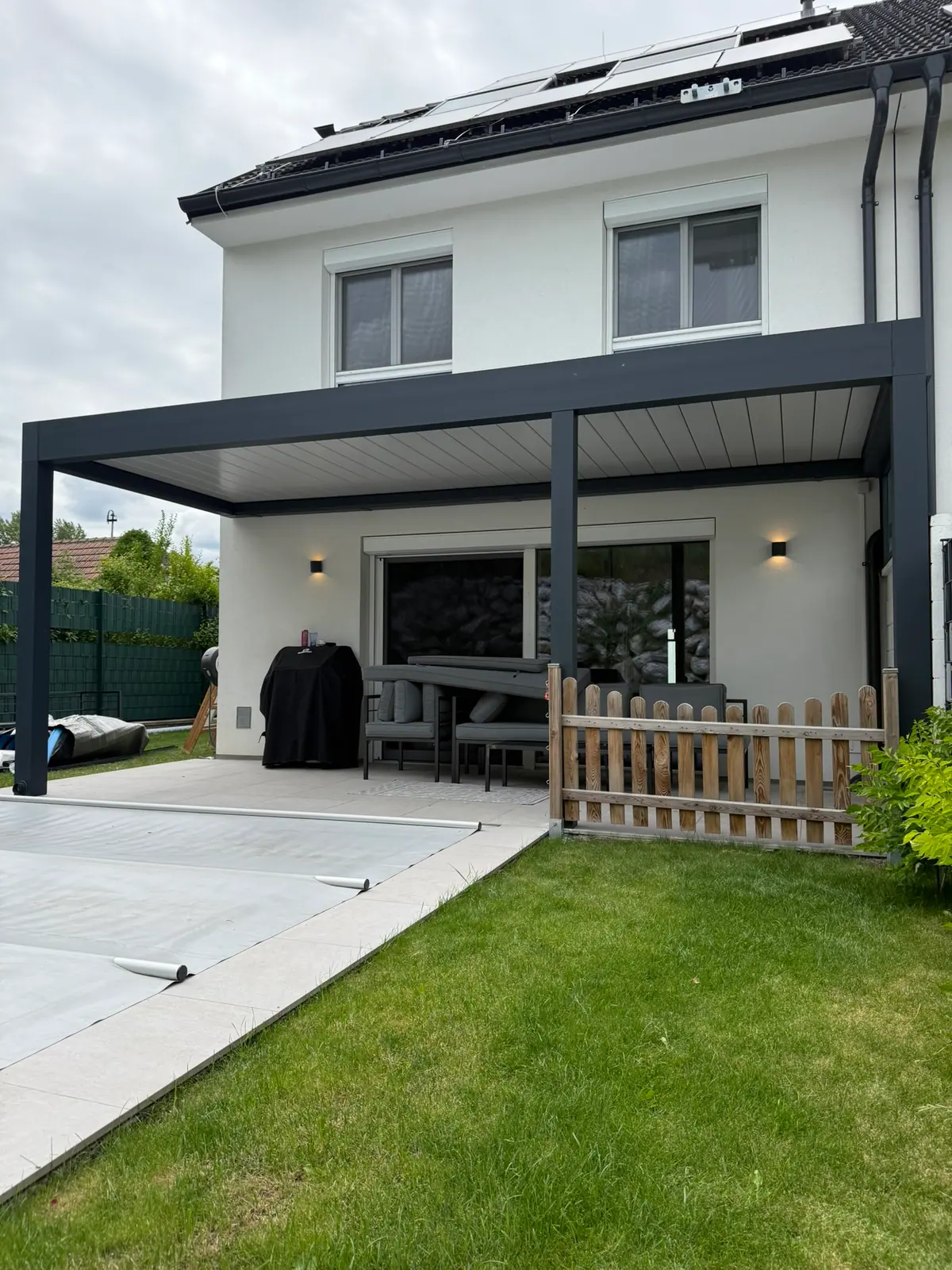 Pergola mit Lamellendach an einem Einfamilienhaus mit Pool und Garten
