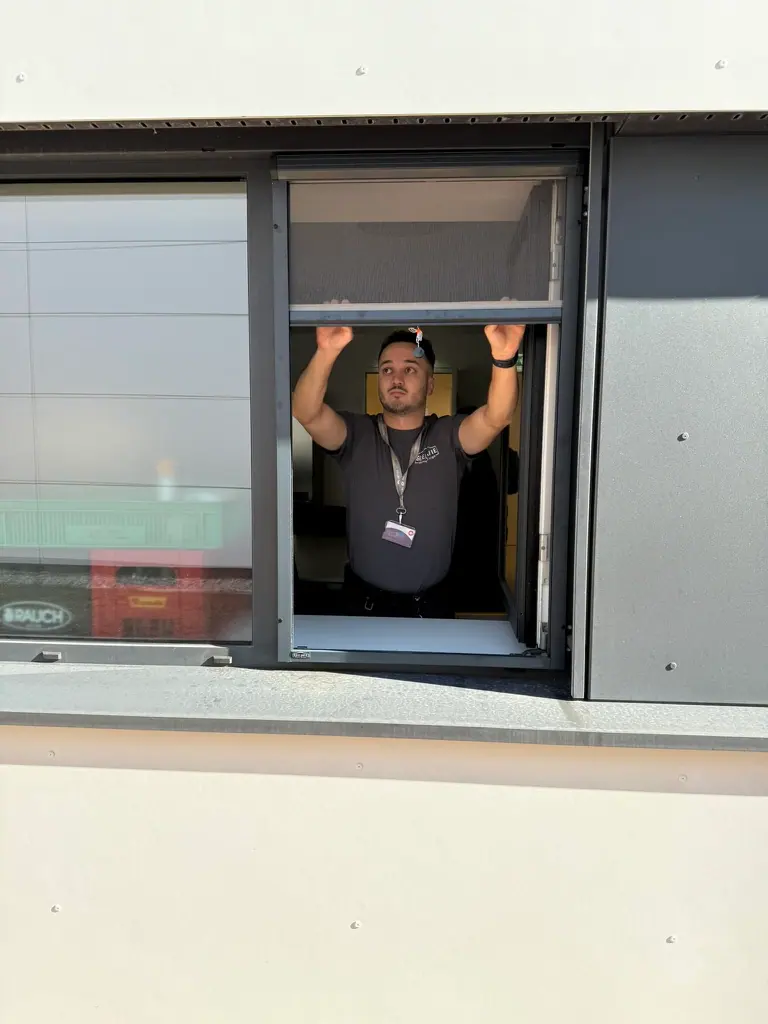 Monteur zeigt ein Fliegengitter-Rollo im Fenster