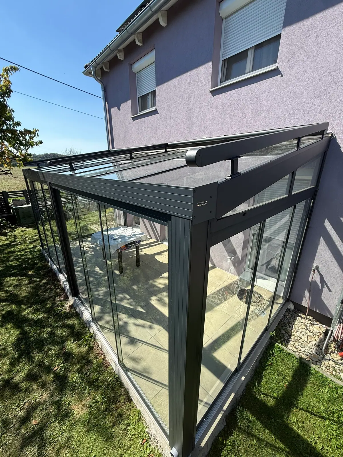 Sommergarten mit schrägem Glasdach und Glasschiebewänden an einem Wohnhaus