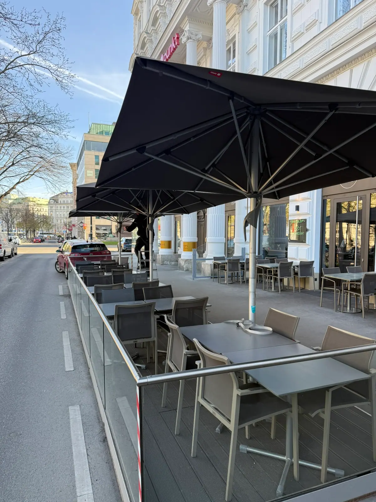 Sonnenschirm über den Tischen eines Gastgartens an der Straße