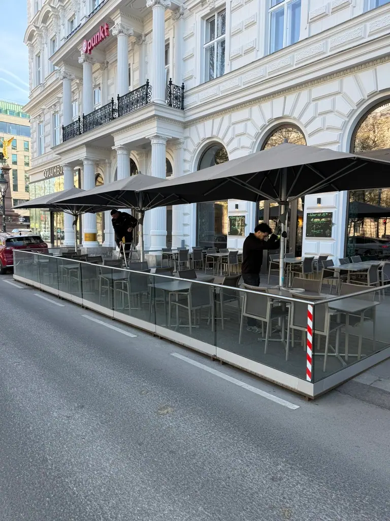 Gastgarten mit großen Sonnenschirmen und Glas-Windschutz
