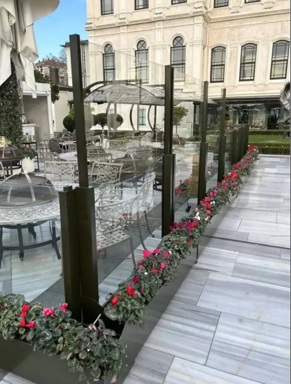 Gläserne Windschutzwände mit Blumenkästen entlang eines Gastgartens